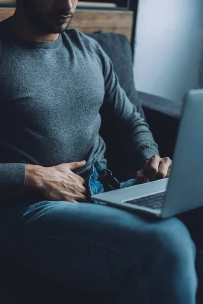 Cropped view of young man masturbating and watching pornography on laptop on couch — Stock Photo