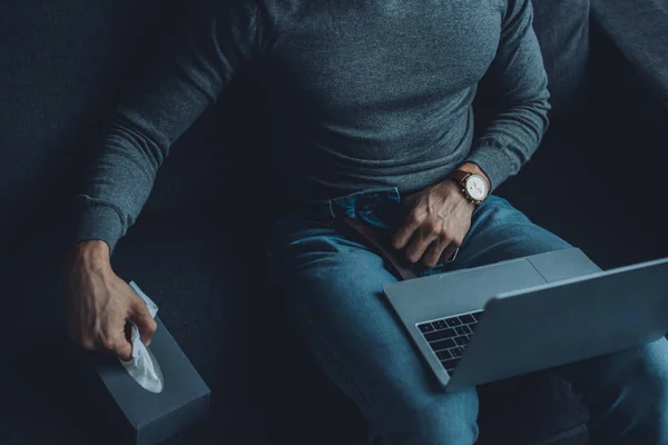 Ausgeschnittene Ansicht eines Mannes, der Serviette aus Schachtel nimmt, während er Pornografie auf dem Laptop auf der Couch anschaut — Stockfoto