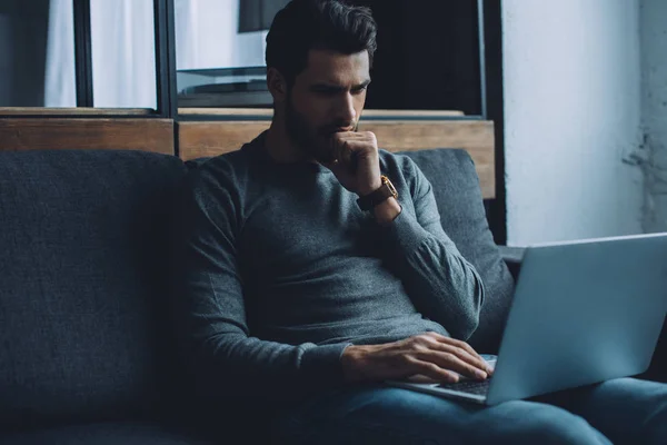 Bonito homem com a mão perto da boca assistindo pornografia no laptop na sala de estar — Fotografia de Stock