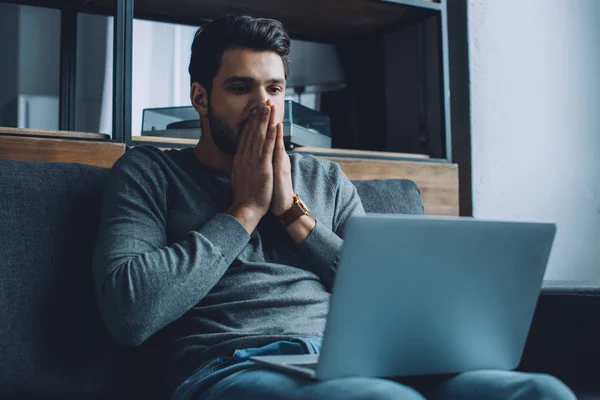 Geschockter Mann mit Händen in Mundnähe schaut Pornografie auf Laptop im Wohnzimmer — Stockfoto