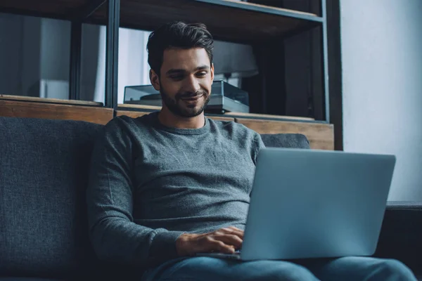 Young man smiling while watching pornography on laptop in living room — Stock Photo