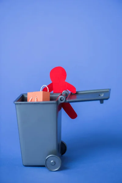 Papel humano cerca de un pequeño bote de basura con bolsa de compras - foto de stock
