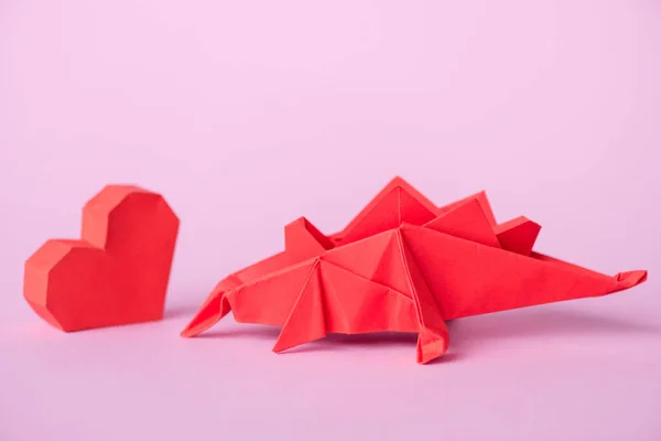 Червоне паперове серце біля орігамі динозавра на рожевому — стокове фото