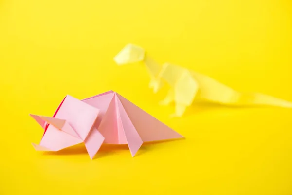 Fuoco selettivo del rinoceronte di carta rosa vicino al dinosauro origami sul giallo — Foto stock
