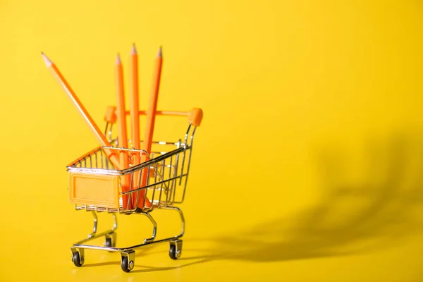Selective focus of toy shopping cart with pencils on yellow — Stock Photo