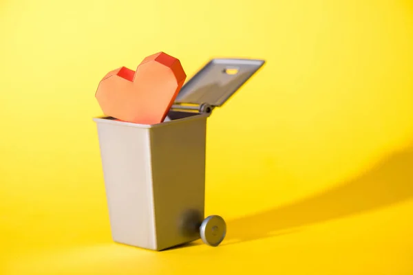 Бумажное сердце в маленькой мусорке на желтом — стоковое фото
