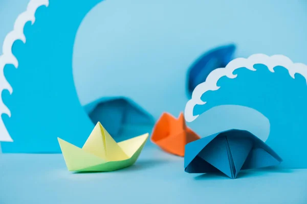 Enfoque selectivo de barcos de papel de colores cerca de las olas en azul - foto de stock