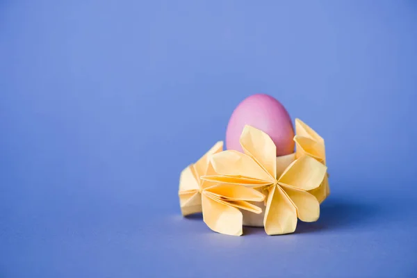 Декоративні квіти орігамі біля великодніх яєць на синьому — стокове фото