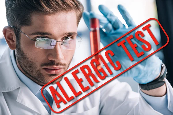 Selective focus of bearded allergist in glasses holding test tube with red liquid with allergic test illustration — Stock Photo