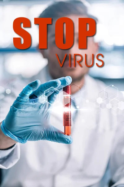 Enfoque selectivo del epidemiólogo que sostiene el tubo de ensayo con líquido rojo y detener la ilustración del virus - foto de stock
