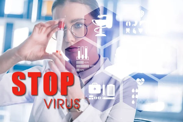 Selective focus of beautiful epidemiologist in glasses holding test tube near stop virus illustration — Stock Photo