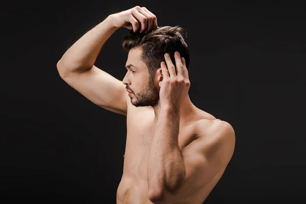 Bearded handsome nude man combing hair isolated on black — Stock Photo