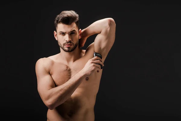 Sexy naked man applying deodorant on armpit isolated on black — Stock Photo