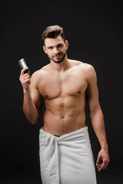 Sexy smiling man holding deodorant isolated on black — Stock Photo