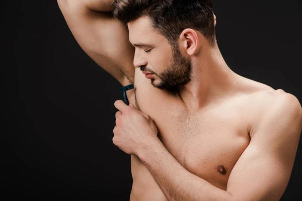 Брюнетка обнаженная мужчина бритья подмышки с бритвой изолированы на черный — стоковое фото