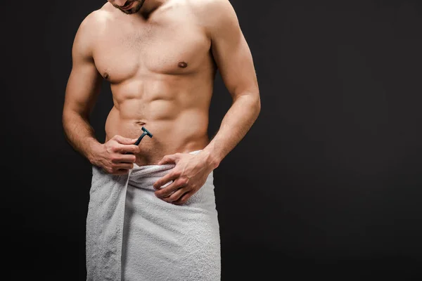 Обрезанный вид мускулистого мужчины без рубашки в полотенце с бритвой, изолированной на черном — стоковое фото