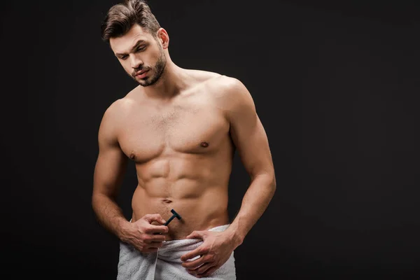 Handsome muscular shirtless man in towel holding razor isolated on black — Stock Photo