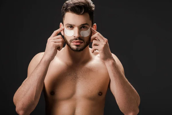 Brunette nude man applying eye patches on face isolated on black — Stock Photo