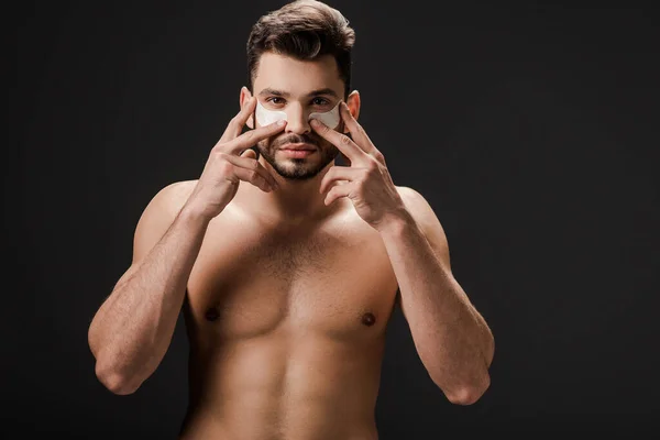 Barbuto sexy uomo nudo applicare macchie oculari sul viso isolato su nero — Foto stock