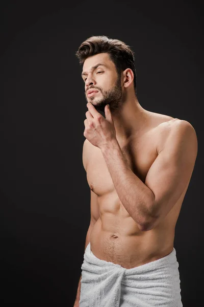 Hombre sexy pensativo en toalla tocando la barba aislado en negro — Stock Photo