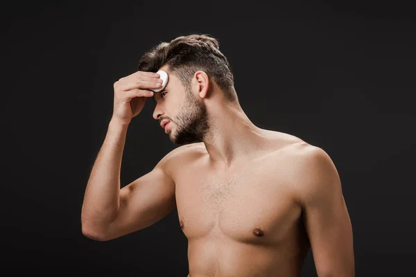 Sexy naked man using cosmetic cotton pad isolated on black — Stock Photo