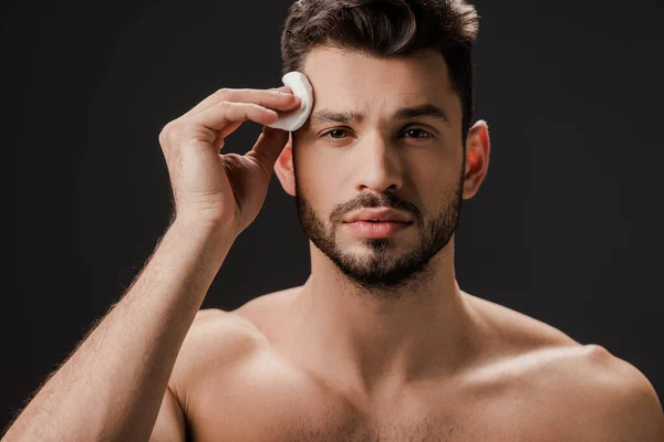 Bel homme nu utilisant un tampon cosmétique en coton isolé sur noir — Photo de stock