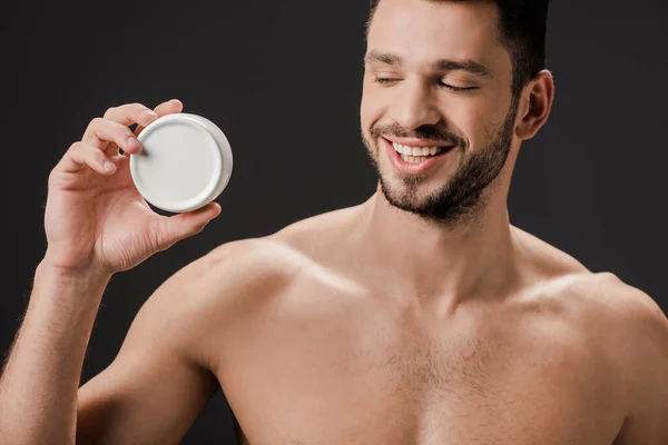 Cheerful naked man holding plastic container with face cream isolated on grey — Stock Photo