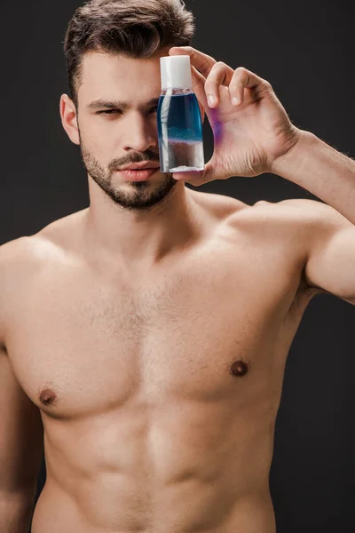 Sexy naked man holding bottle with cosmetic liquid isolated on black — Stock Photo