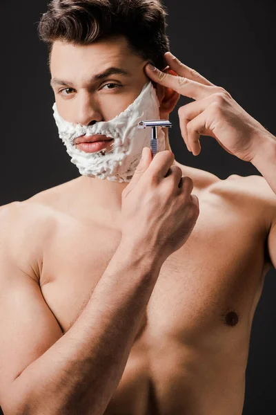 Sexy nude bearded man shaving face with razor isolated on black — Stock Photo