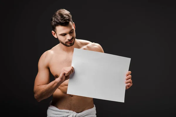 Sexy uomo senza maglietta in asciugamano in possesso di cartello bianco isolato su nero — Foto stock