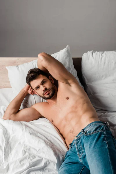 Sexy shirtless man in jeans lying on bed on grey — Stock Photo