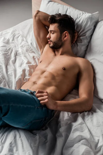Seductive shirtless man in jeans lying on bed on grey — Stock Photo
