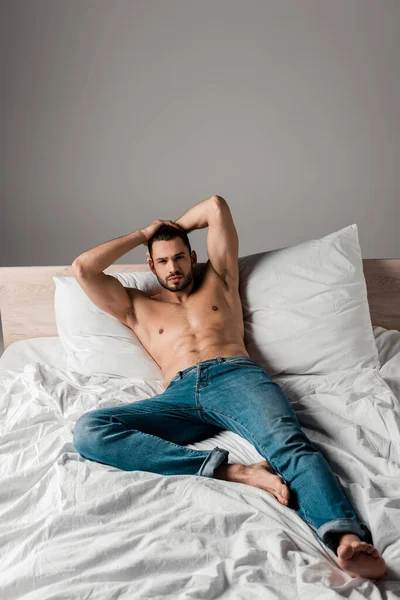 Сексуальный бородатый мужчина в джинсах лежит на кровати на серой — стоковое фото
