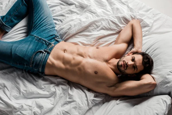 Vista dall'alto di bel uomo sexy senza camicia sdraiato sul letto isolato sul grigio — Foto stock