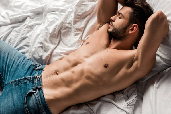 Vista dall'alto di bel uomo sexy senza camicia in jeans sdraiato sul letto — Foto stock