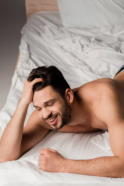 Sexy smiling man in jeans lying on bed on grey — Stock Photo