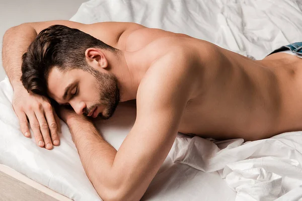 Handsome shirtless man in jeans sleeping on bed isolated on grey — Stock Photo