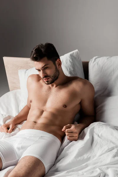 Barbudo guapo sexy hombre acostado en la cama en gris - foto de stock