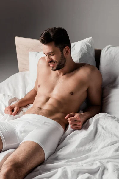 Smiling bearded handsome sexy man lying on bed on grey — Stock Photo