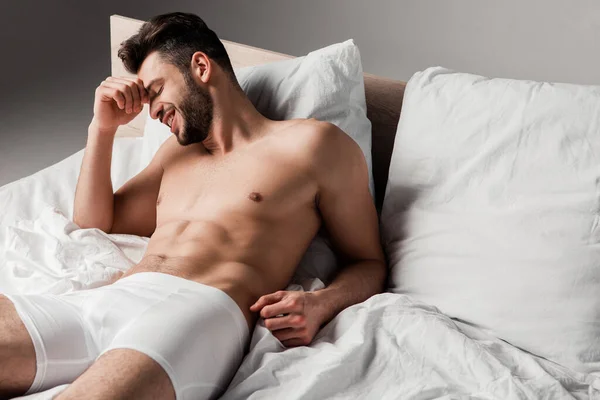 Laughing handsome sexy man lying on bed on grey — Stock Photo