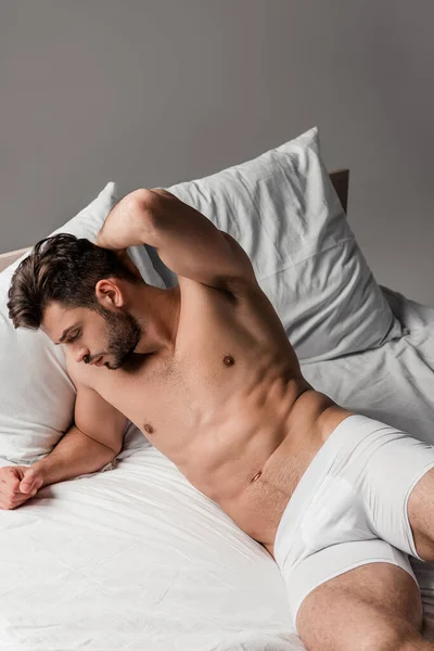 Bearded handsome seductive man lying on bed on grey — Stock Photo