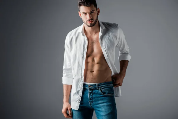 Sexy brunette man in white shirt and jeans on grey — Stock Photo