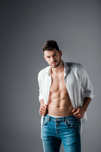 Sexy muscular man in white shirt and jeans on grey — Stock Photo