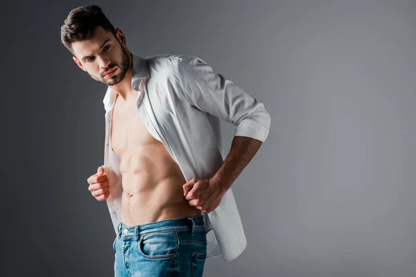 Sexy hombre guapo en camisa blanca y jeans en gris - foto de stock
