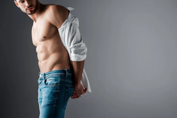 Sexy muskulöser Mann in weißem Hemd und Jeans auf grau — Stockfoto