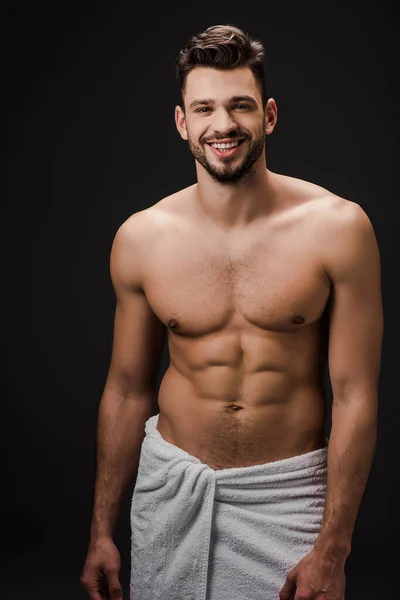 Sonriente sexy musculoso hombre en toalla aislado en negro - foto de stock