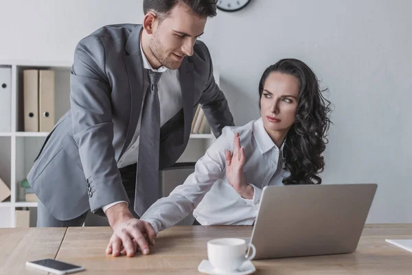 Angry secretary showing stop gesture to businessman touching her hand — Stock Photo