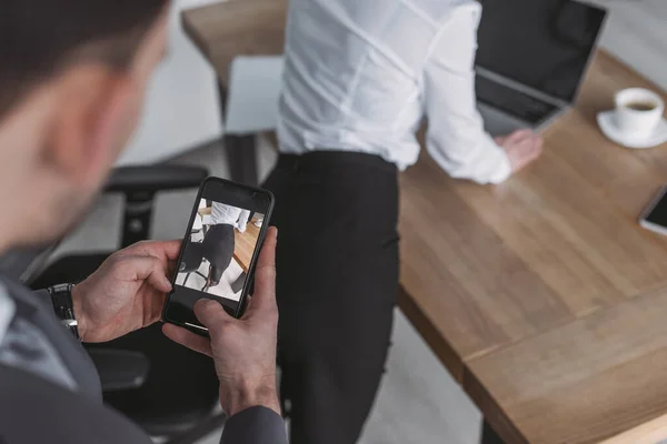 Selective focus of businessman taking photo of buttocks of secretary on smartphone — Stock Photo