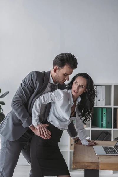 Handsome businessman molesting angry secretary in office — Stock Photo
