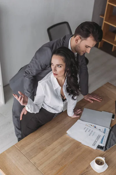 High angle view of businessman touching buttocks of angry secretary standing at workplace — Stock Photo
